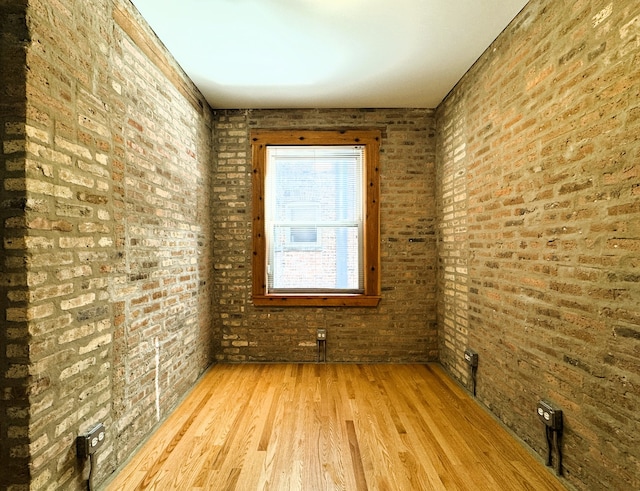 unfurnished room featuring light hardwood / wood-style floors and brick wall