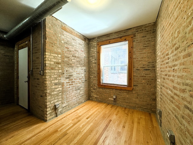 spare room with light hardwood / wood-style flooring and brick wall