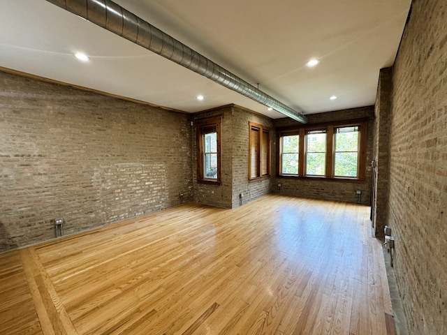 unfurnished living room with brick wall and light wood-type flooring