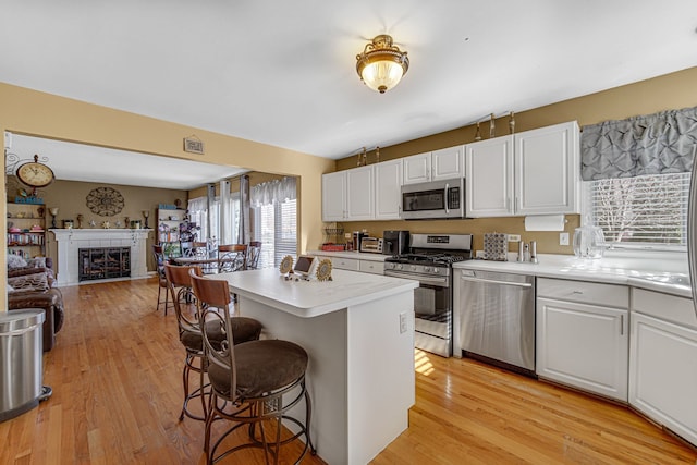 kitchen with appliances with stainless steel finishes, a breakfast bar, a center island, light hardwood / wood-style floors, and white cabinetry