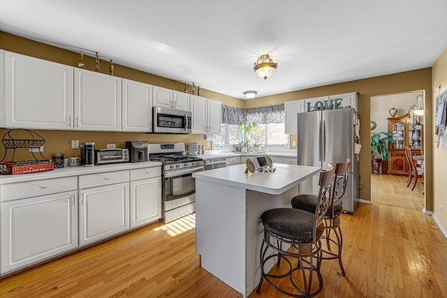 kitchen featuring white cabinetry, a center island, stainless steel appliances, a kitchen bar, and light wood-type flooring