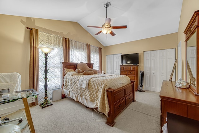 bedroom with light carpet, multiple closets, lofted ceiling, and ceiling fan