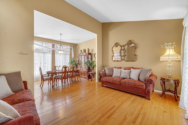 living room featuring light hardwood / wood-style flooring, vaulted ceiling, and a notable chandelier