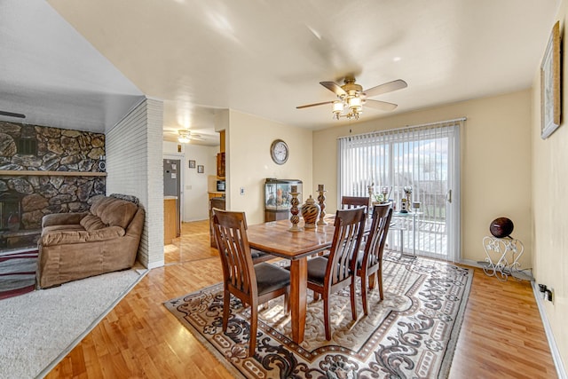 dining area with a fireplace, light wood-type flooring, and ceiling fan