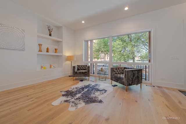 sitting room featuring built in shelves and light hardwood / wood-style flooring