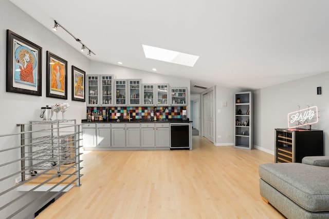 bar featuring wine cooler, light hardwood / wood-style flooring, backsplash, gray cabinets, and vaulted ceiling with skylight