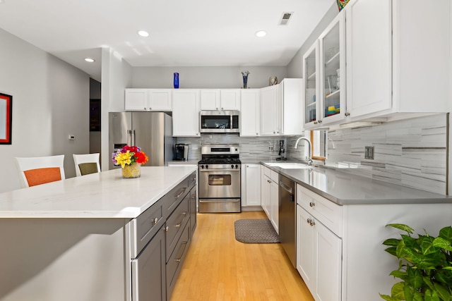 kitchen featuring sink, appliances with stainless steel finishes, light hardwood / wood-style floors, a kitchen bar, and white cabinetry