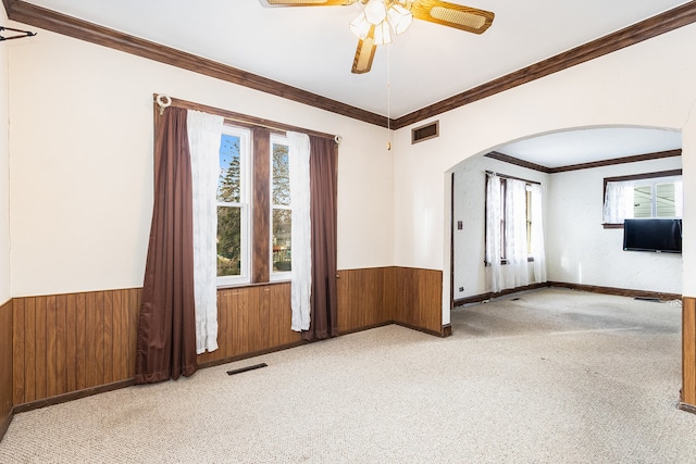 carpeted spare room with wooden walls, ceiling fan, and ornamental molding