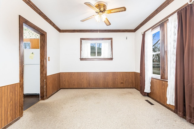 carpeted spare room with ceiling fan, crown molding, and wooden walls