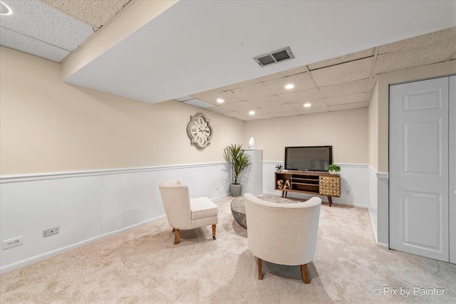 living area featuring a paneled ceiling and carpet flooring