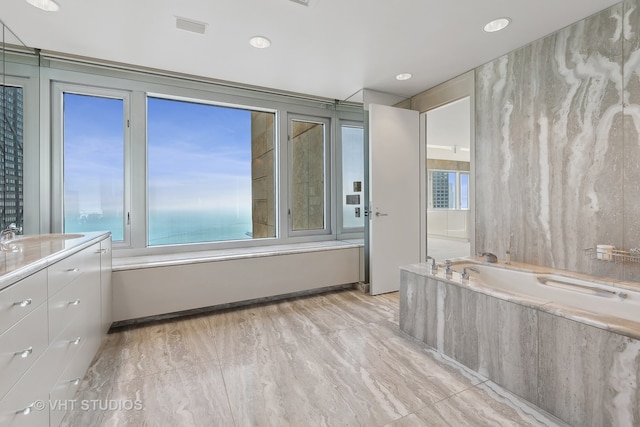 bathroom featuring a tub to relax in, a water view, and sink