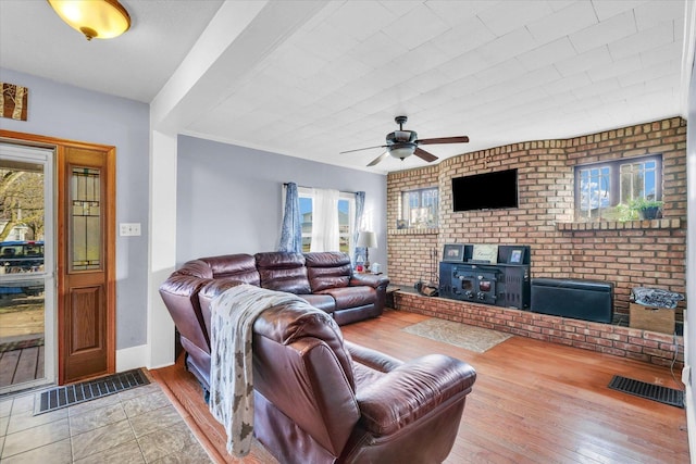 living room with hardwood / wood-style flooring, ceiling fan, a wood stove, and brick wall