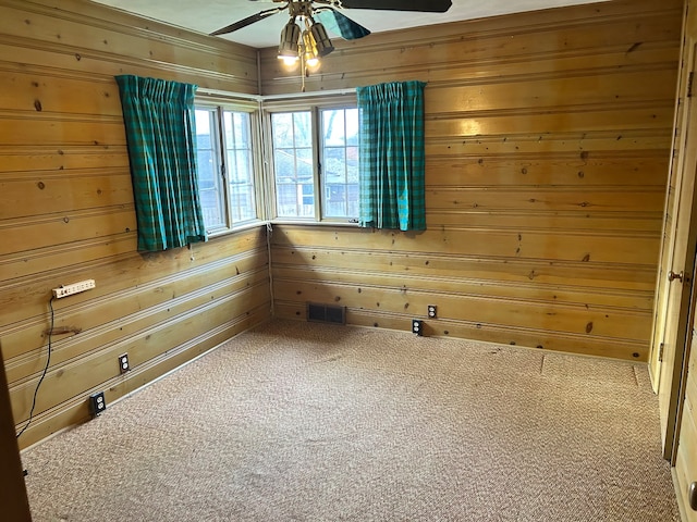 unfurnished room featuring carpet flooring, wooden walls, and ceiling fan