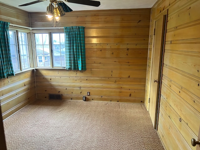 empty room featuring carpet flooring, ceiling fan, and wood walls