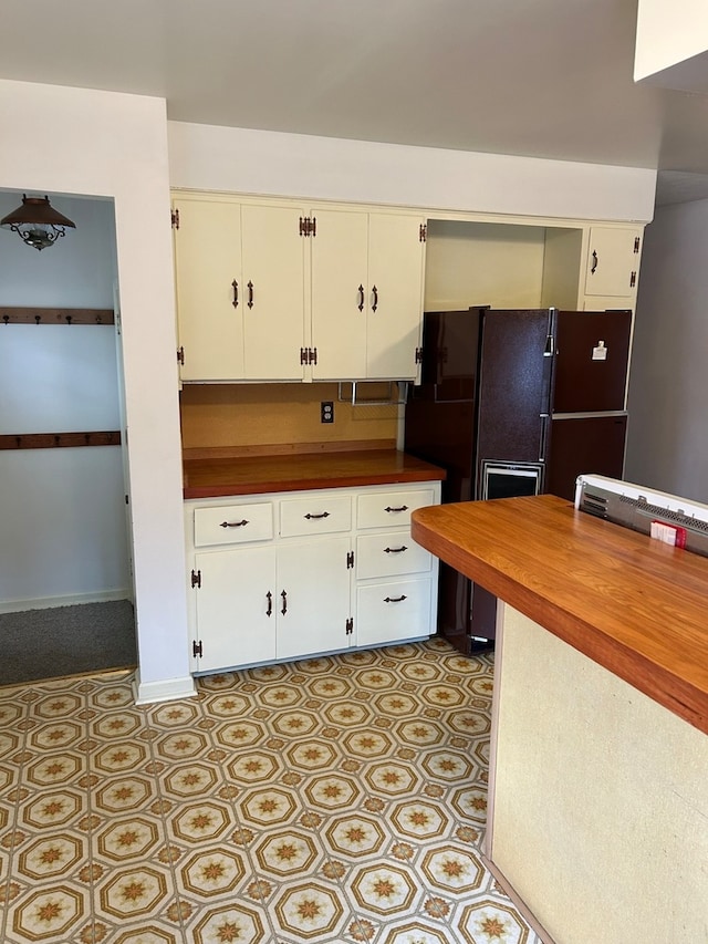 kitchen featuring butcher block counters, black fridge, and white cabinetry