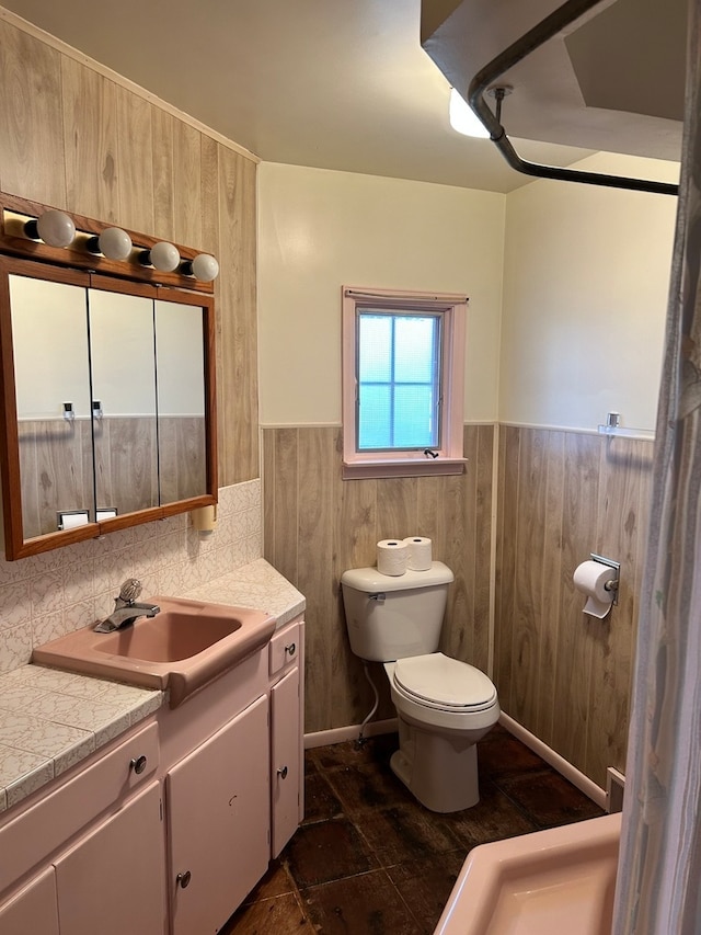 bathroom featuring vanity, toilet, and wooden walls