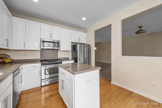 kitchen with a center island, stainless steel appliances, white cabinetry, and light hardwood / wood-style flooring