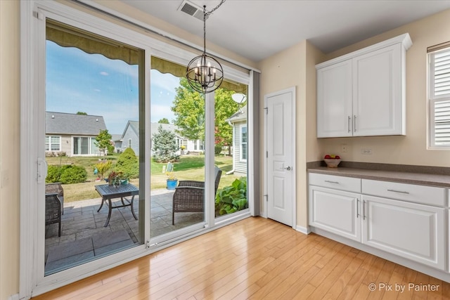 doorway to outside with a healthy amount of sunlight, light wood-type flooring, and an inviting chandelier