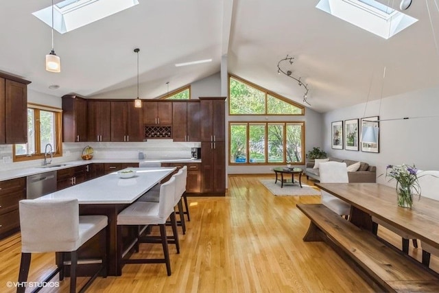 kitchen featuring lofted ceiling with skylight, sink, stainless steel dishwasher, a kitchen island, and pendant lighting