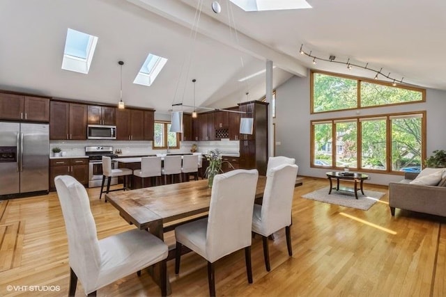 dining space with beam ceiling, high vaulted ceiling, and light wood-type flooring