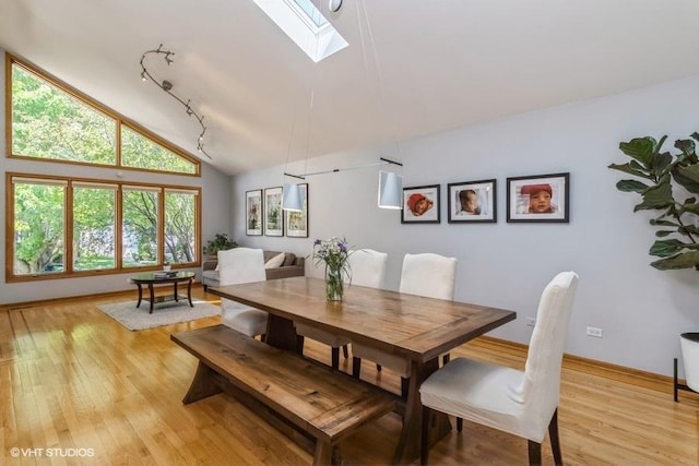 dining space with lofted ceiling with skylight, rail lighting, and light wood-type flooring