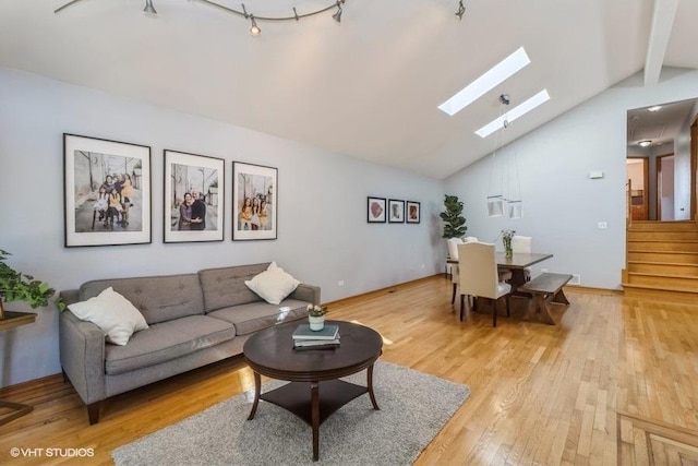 living room featuring rail lighting, a skylight, high vaulted ceiling, light hardwood / wood-style flooring, and beamed ceiling