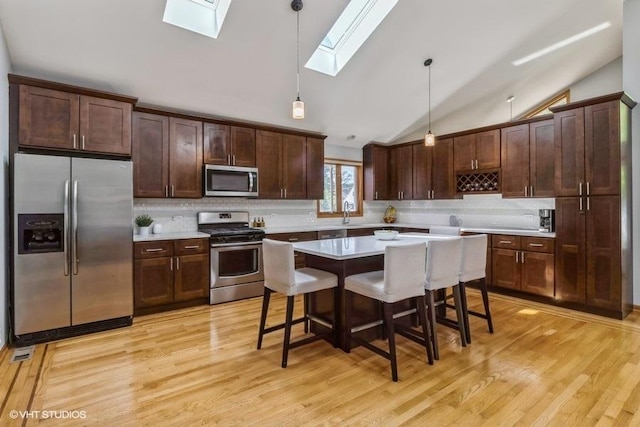 kitchen with a kitchen breakfast bar, hanging light fixtures, a center island, stainless steel appliances, and light hardwood / wood-style flooring