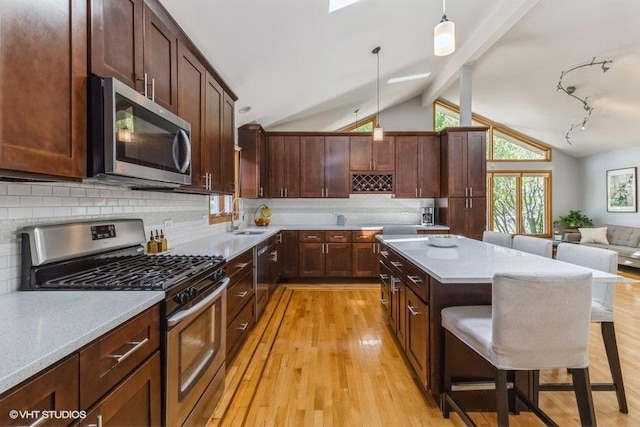 kitchen featuring appliances with stainless steel finishes, a breakfast bar, lofted ceiling with beams, sink, and hanging light fixtures