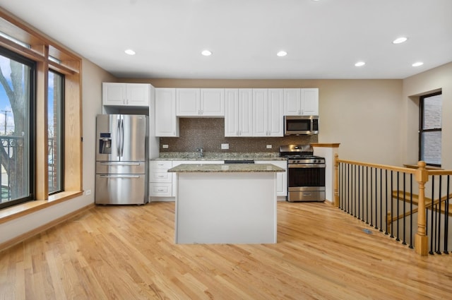 kitchen with light stone countertops, white cabinetry, light hardwood / wood-style floors, decorative backsplash, and appliances with stainless steel finishes