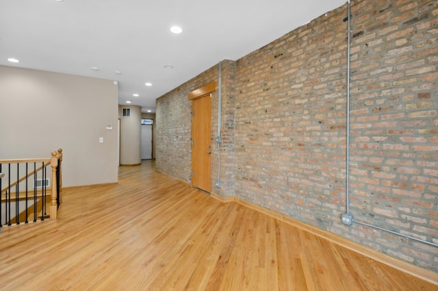 unfurnished room featuring light hardwood / wood-style floors and brick wall