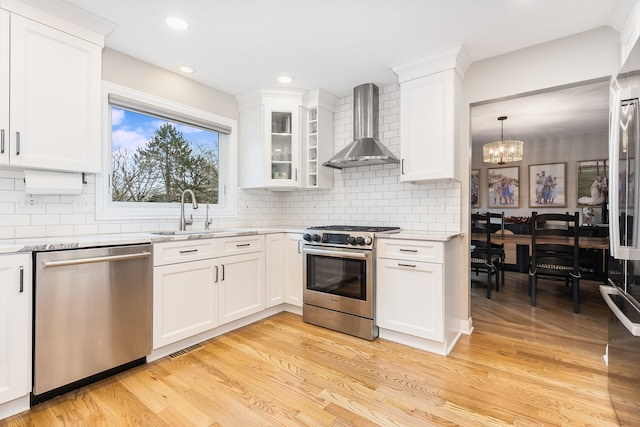 kitchen featuring appliances with stainless steel finishes, sink, wall chimney range hood, light hardwood / wood-style floors, and white cabinetry