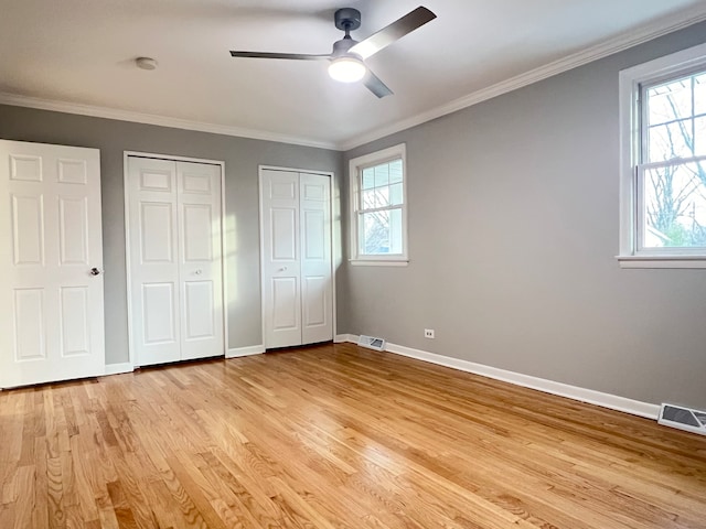 unfurnished bedroom with ceiling fan, light hardwood / wood-style floors, ornamental molding, and two closets