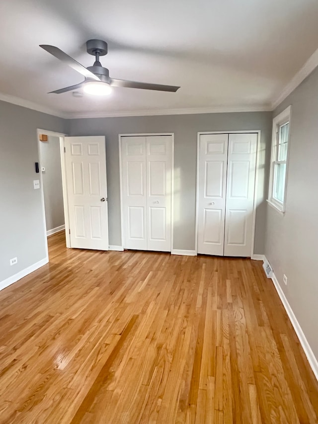 unfurnished bedroom with light wood-type flooring, two closets, ceiling fan, and crown molding