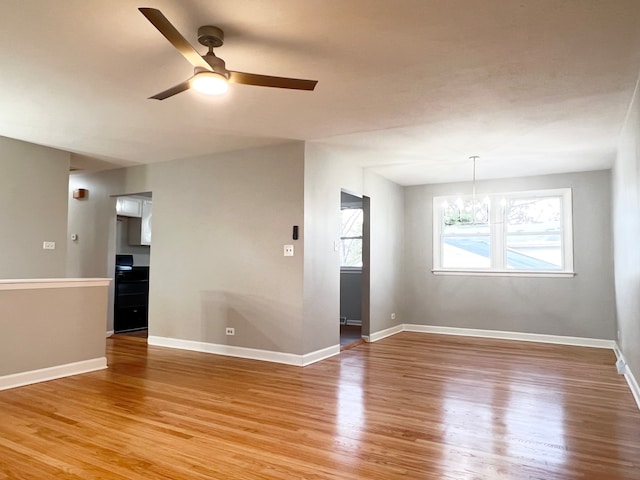 empty room with wood-type flooring and ceiling fan with notable chandelier