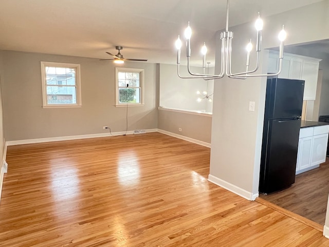 unfurnished dining area featuring ceiling fan with notable chandelier and light hardwood / wood-style flooring