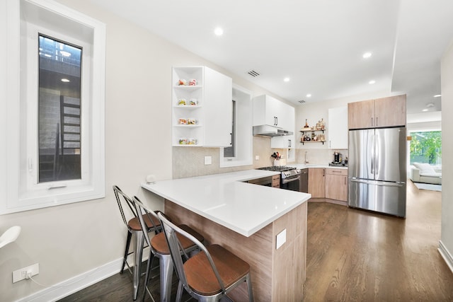 kitchen featuring light brown cabinets, stainless steel appliances, dark hardwood / wood-style floors, kitchen peninsula, and a breakfast bar area