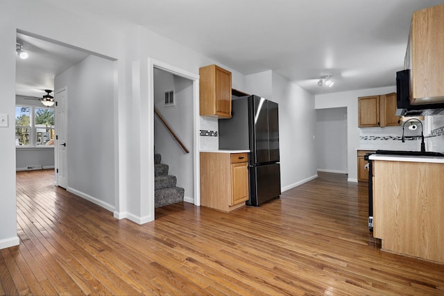 kitchen with decorative backsplash, black fridge, ceiling fan, sink, and light hardwood / wood-style floors