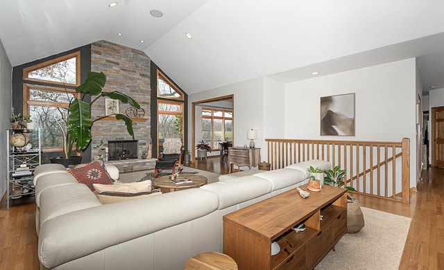 living room featuring a stone fireplace, high vaulted ceiling, a healthy amount of sunlight, and light wood-type flooring