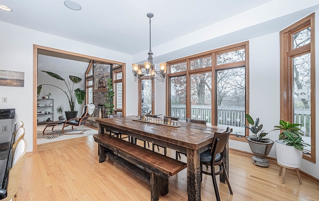 dining area with a healthy amount of sunlight, light wood-type flooring, a fireplace, and a chandelier