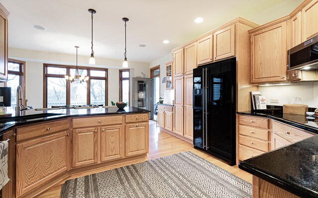 kitchen with light wood-type flooring, black fridge, dark stone countertops, a chandelier, and hanging light fixtures