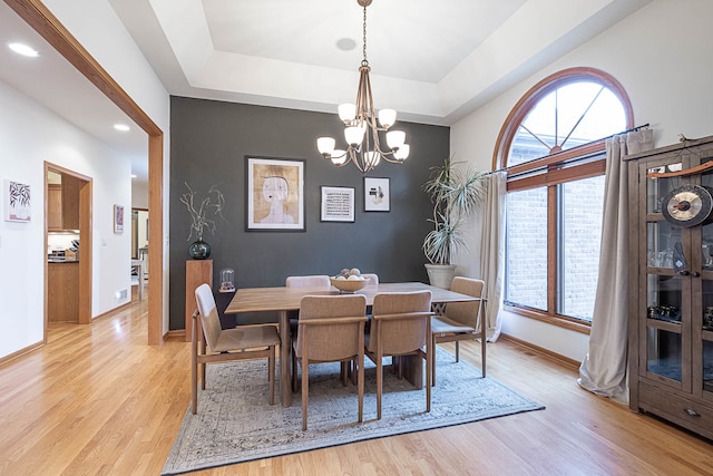 dining area with light wood-type flooring, a tray ceiling, and a notable chandelier