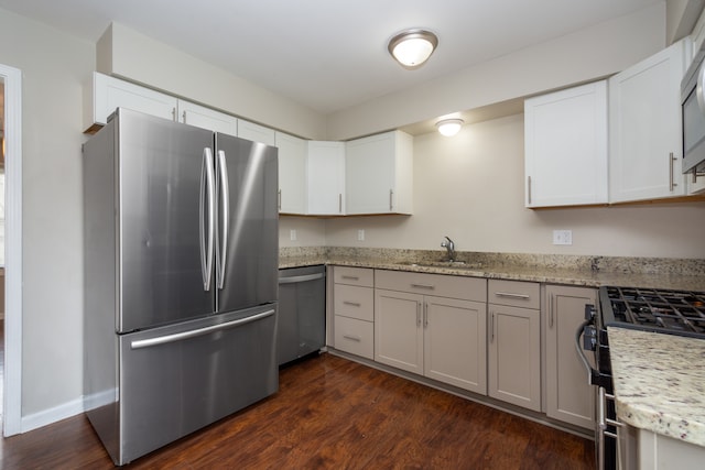 kitchen with light stone countertops, appliances with stainless steel finishes, dark hardwood / wood-style flooring, sink, and white cabinets