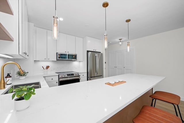 kitchen with hanging light fixtures, sink, a breakfast bar area, white cabinetry, and stainless steel appliances