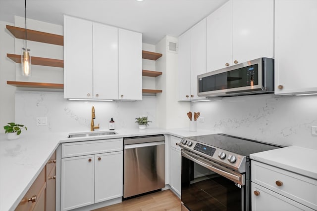 kitchen featuring white cabinetry, sink, light stone counters, light hardwood / wood-style flooring, and appliances with stainless steel finishes