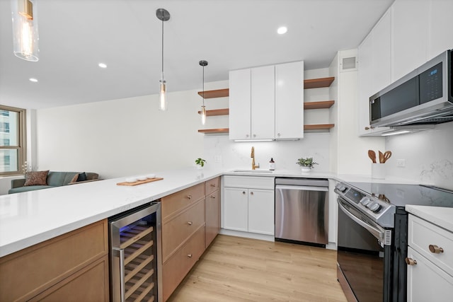 kitchen with pendant lighting, white cabinets, light wood-type flooring, appliances with stainless steel finishes, and beverage cooler