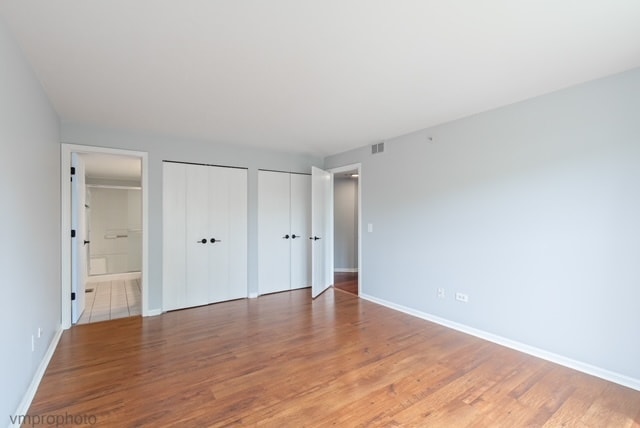 unfurnished bedroom with hardwood / wood-style floors, ensuite bathroom, and two closets