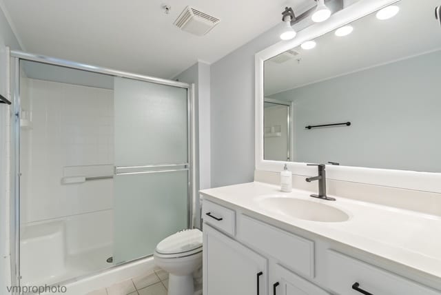 bathroom with tile patterned floors, vanity, an enclosed shower, and toilet