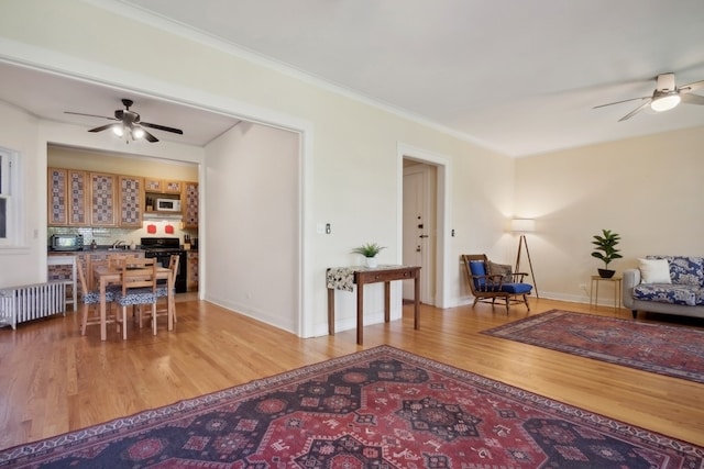 living room featuring hardwood / wood-style floors, ceiling fan, crown molding, and radiator