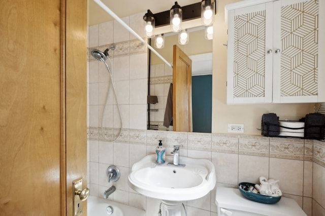 full bathroom with sink, tiled shower / bath combo, toilet, decorative backsplash, and tile walls