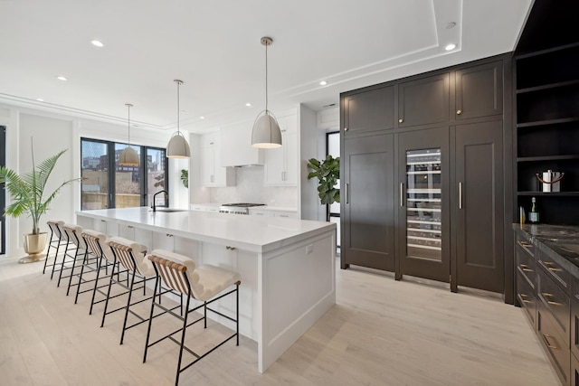 kitchen featuring a spacious island, sink, hanging light fixtures, light wood-type flooring, and white cabinetry